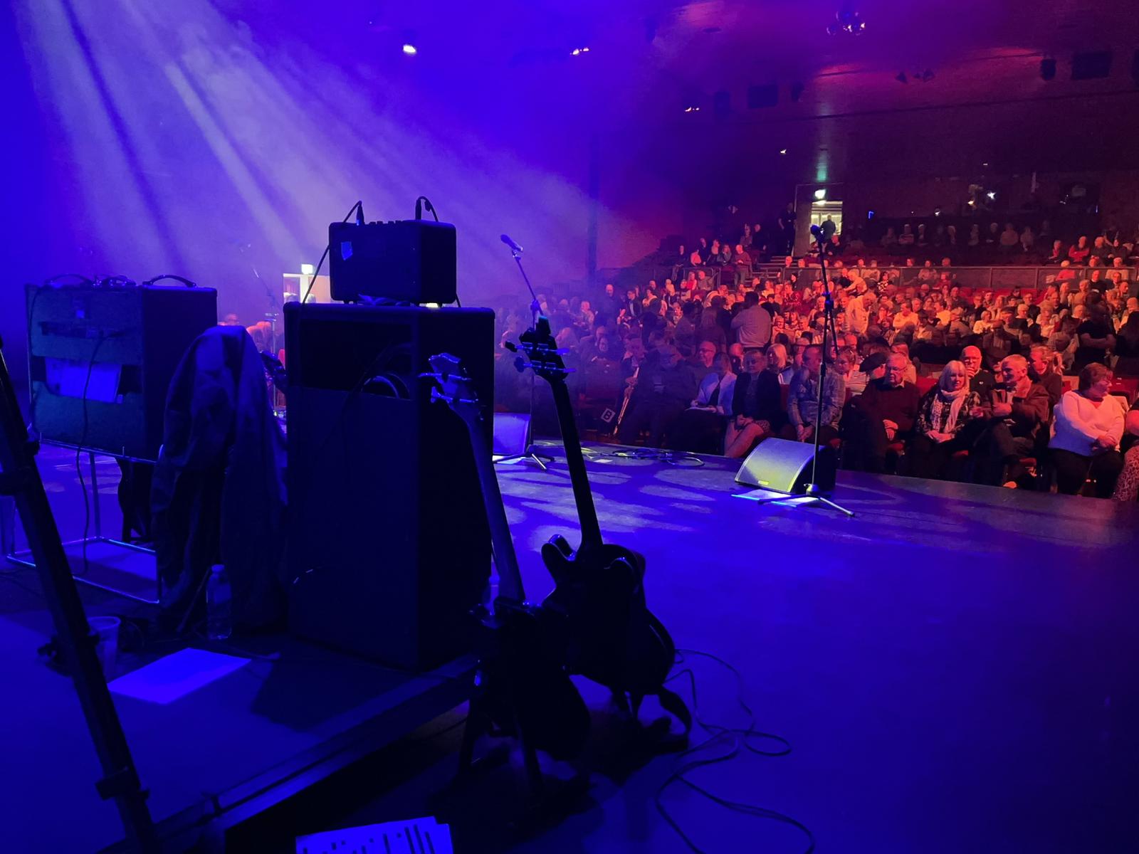 View from the stage out over a packed theatre audience under blue lights
