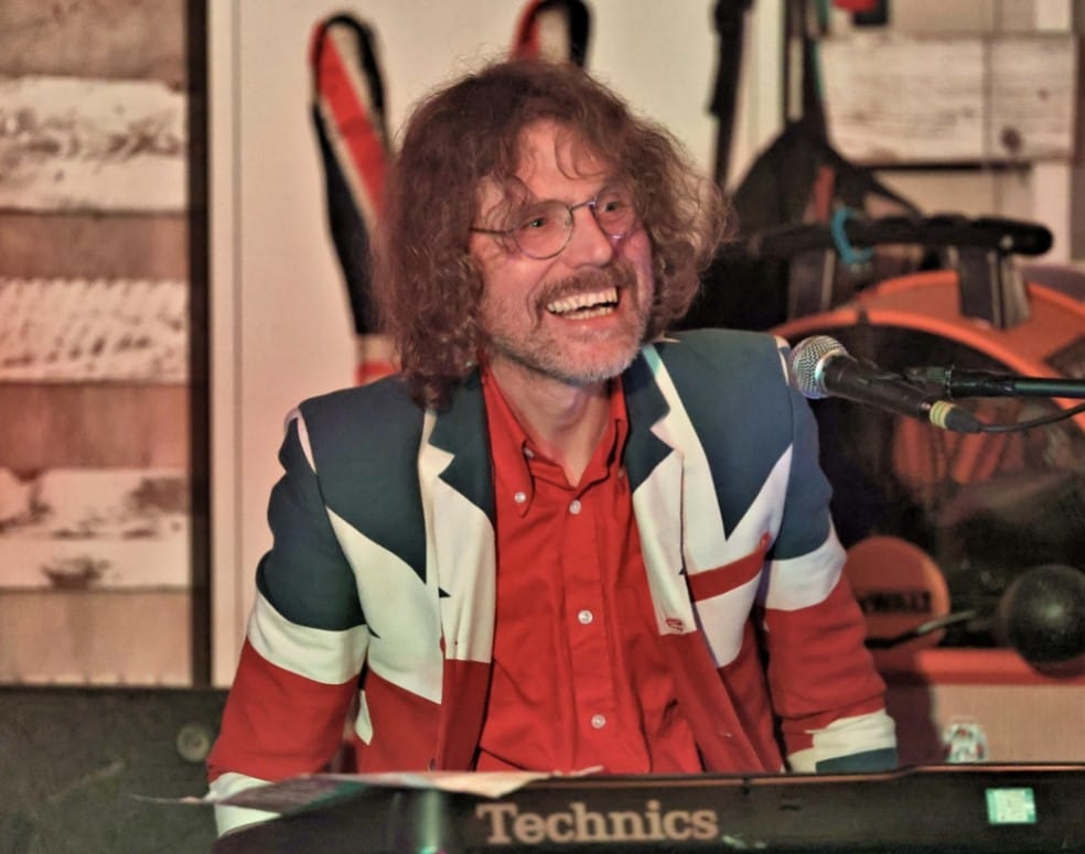 Danny on keys in a Union Jack jacket, smiling at the crowd